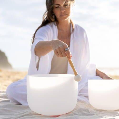 Sound healing practitioner playing a crystal singing bowl during a calming beach meditation session