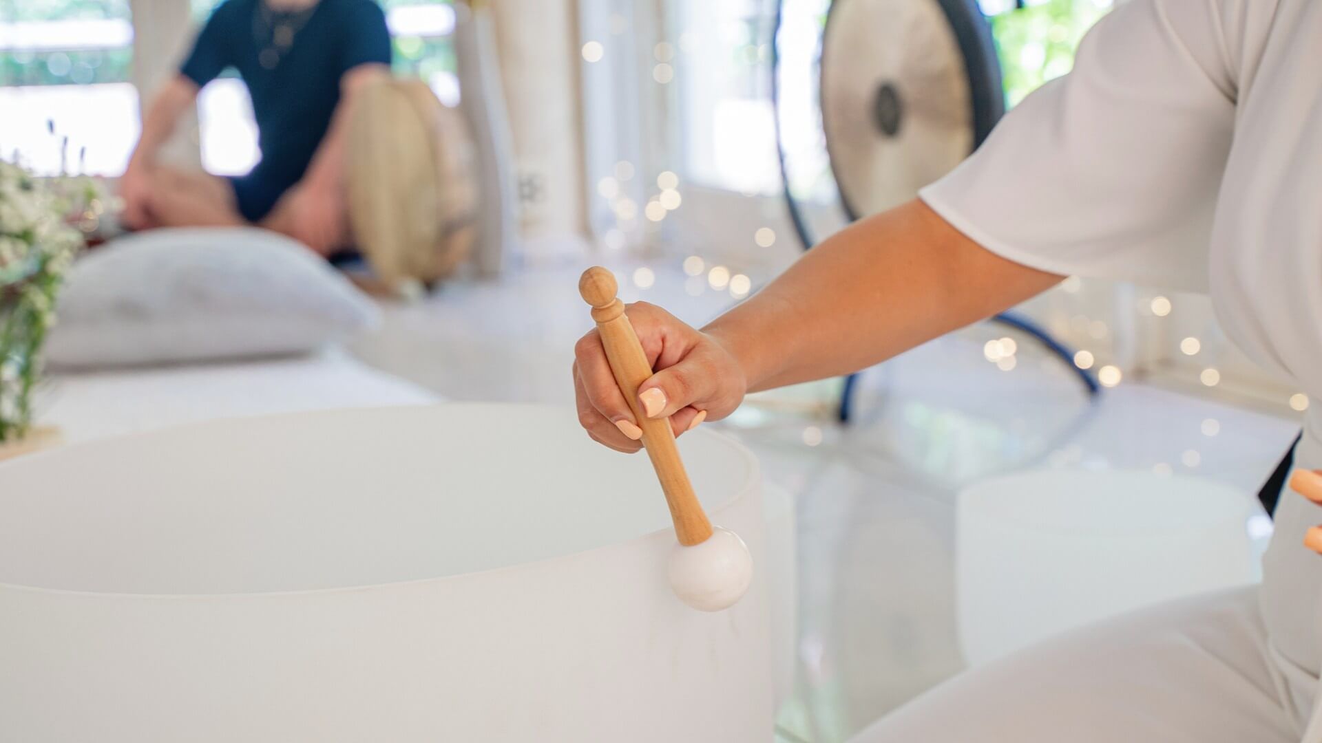Practitioner playing a crystal singing bowl during a sound healing session while participants relax in the background.