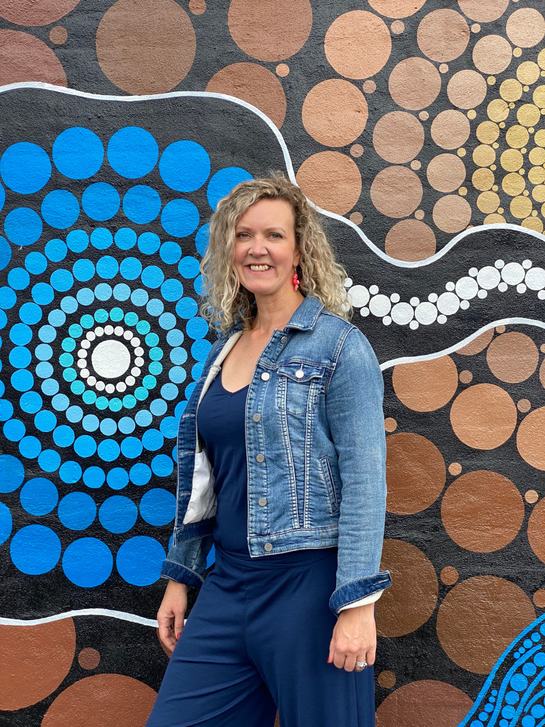 Dr Jo Braid standing in front of wall with indigenous art