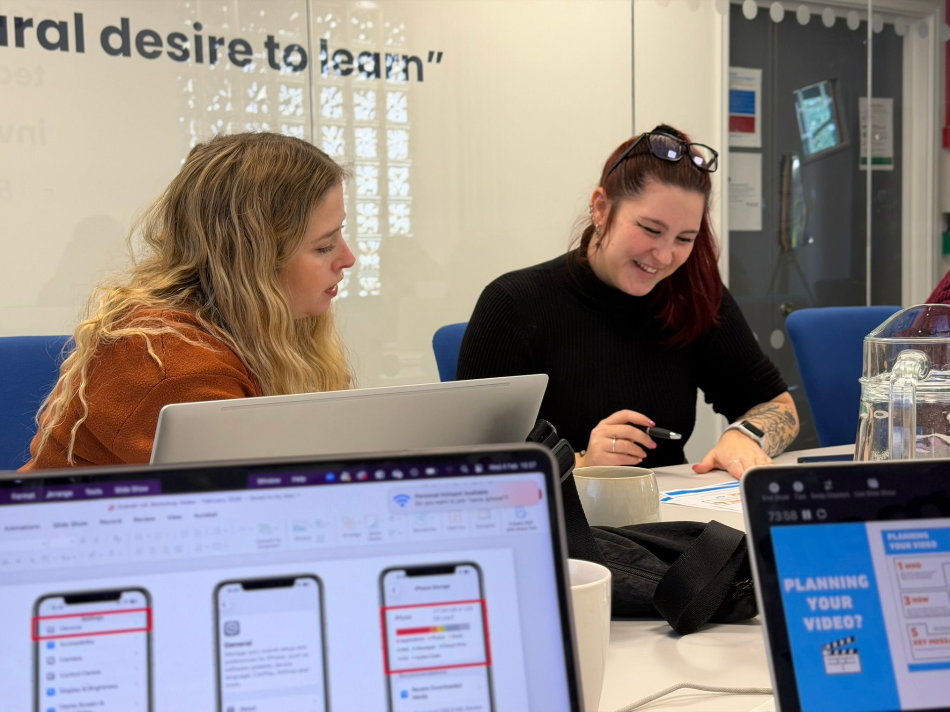 People sitting at a table in a training workshop learning how to use their smartphones to make business videos.. In the foreground are pieces of video making equipment.