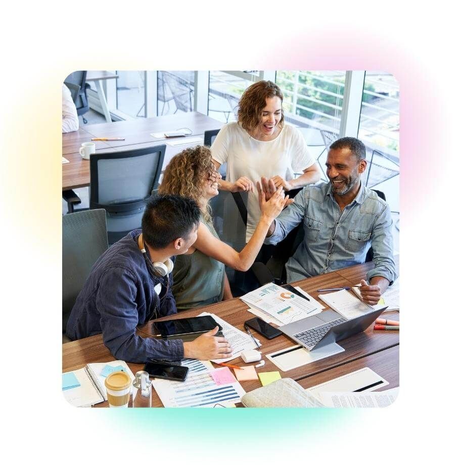 Four colleagues working together at a desk with two people high-fiving.