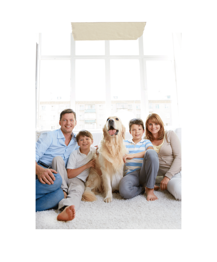 Family of four with a golden retriever sitting together on a white rug in a bright new home with large windows and natural light.