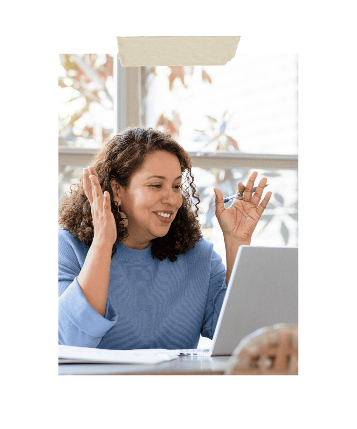Woman smiling and gesturing while on a video call, sitting at a desk with a laptop and papers, representing online coaching, communication, and virtual connection.