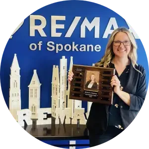 Blonde woman holding an award in front of a RE/MAX sign