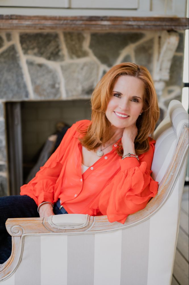 Annie Bauer, host of The Smart Better Life™️ Podcast in orange blouse seated in a chair in front of a fireplace