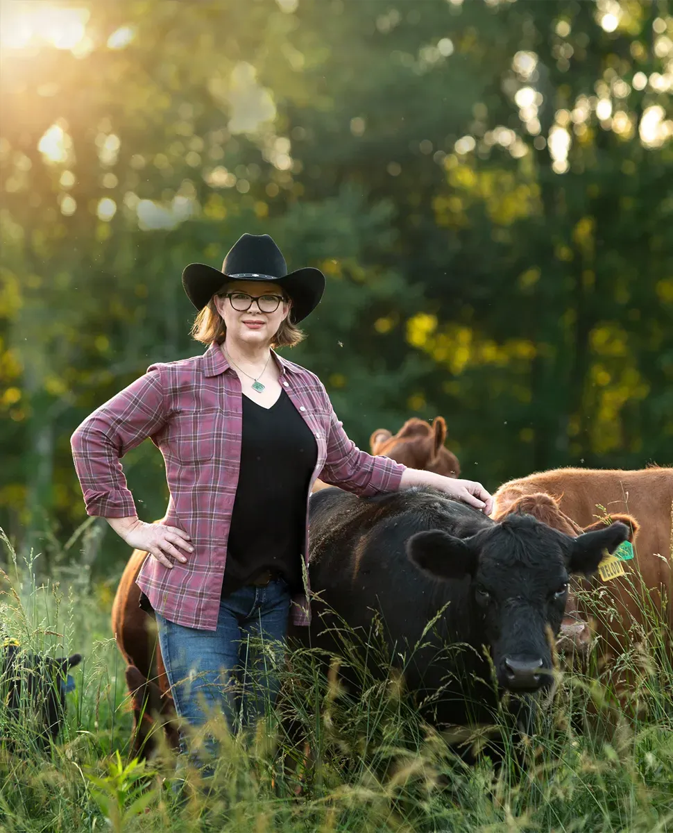 Farmer standing beside a group of Dexter cattle in a sunlit pasture, gently resting a hand on a black cow.