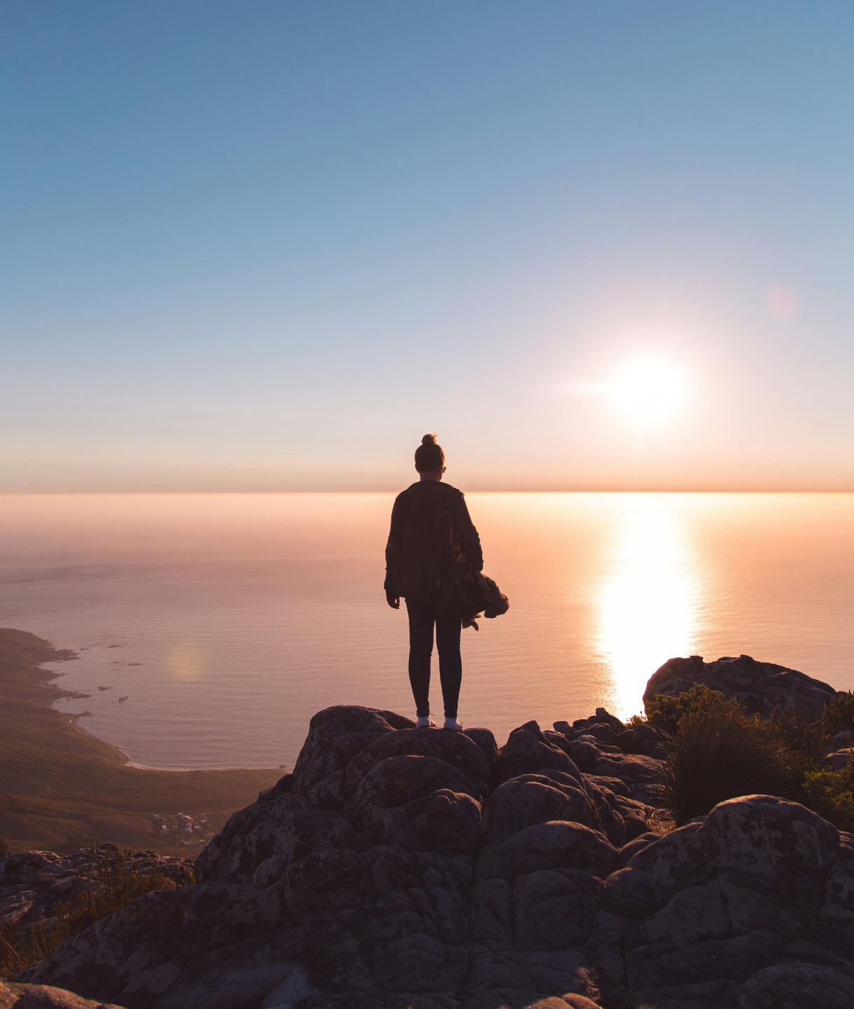 Woman sitting on top of sea cliffs looking out to the horizon 