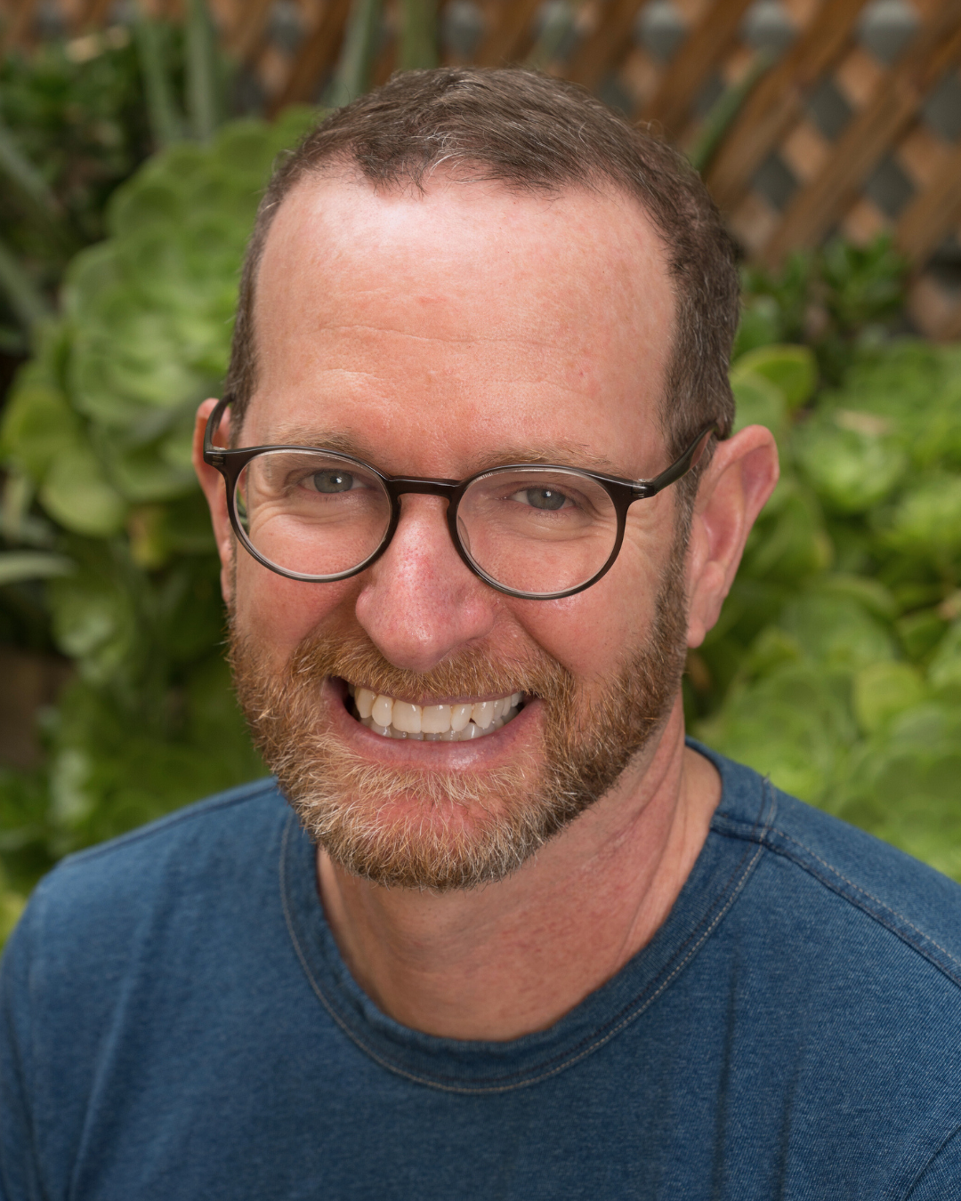 Jivana Heyman wearing brown glasses and a gray shirt.