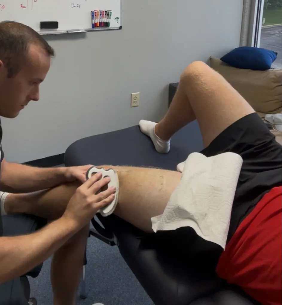 Sports physical therapist applying a post-surgical knee treatment to an athlete during orthopedic rehabilitation in a clinical setting.