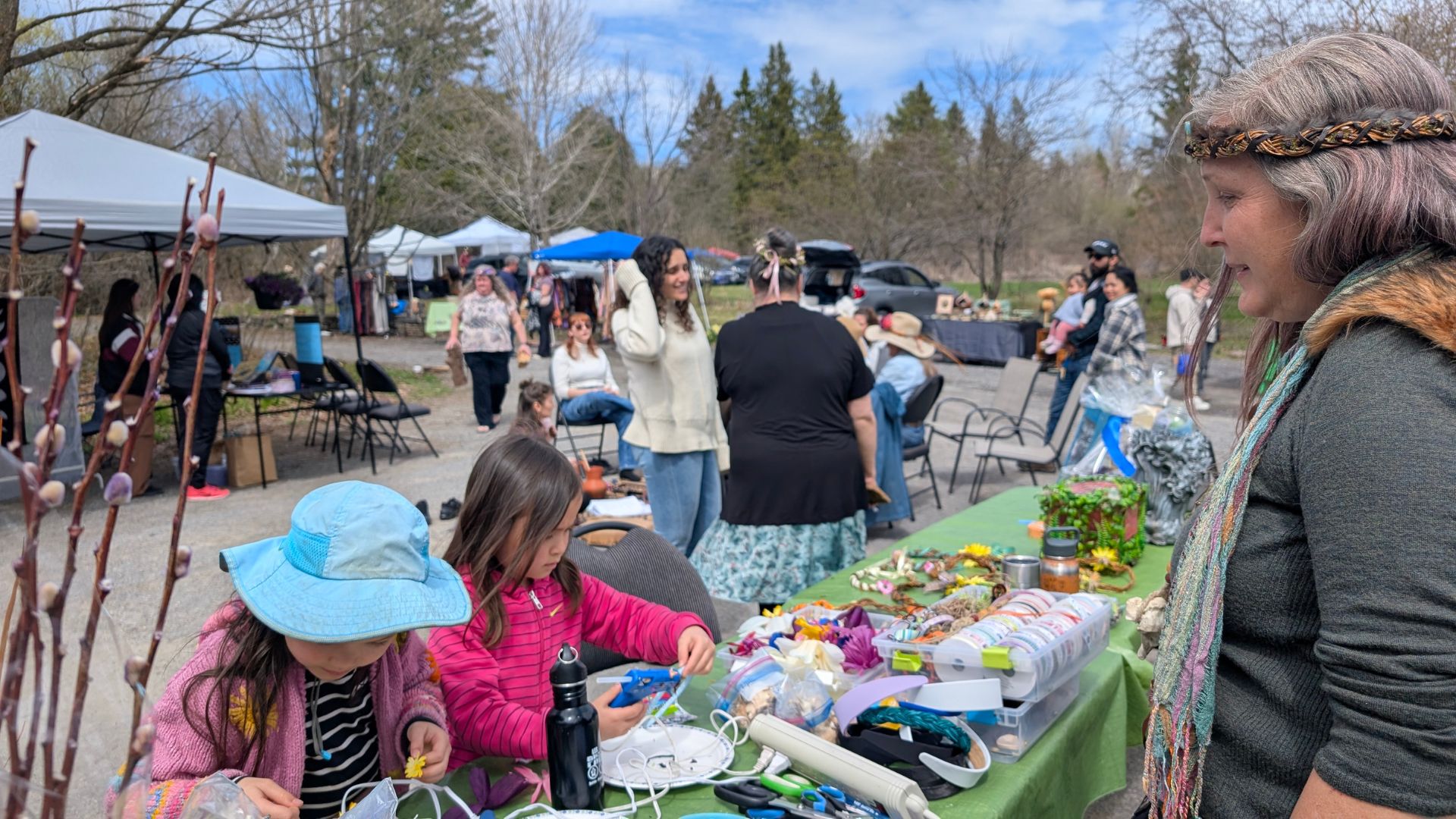 Children making Beltane crafts overseen by a volunteer at an outdoor artisan market