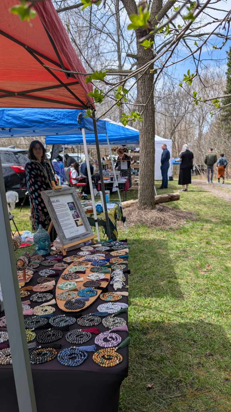 A path set among trees lined with vendor stalls displaying handcrafted items