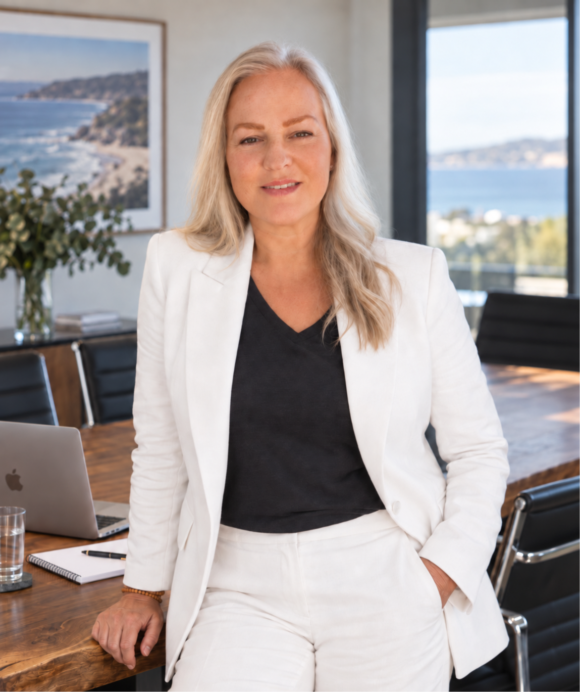 Tania wearing white jacket and black silk top, headshot smiling in boardroom with Apple macbook air laptop