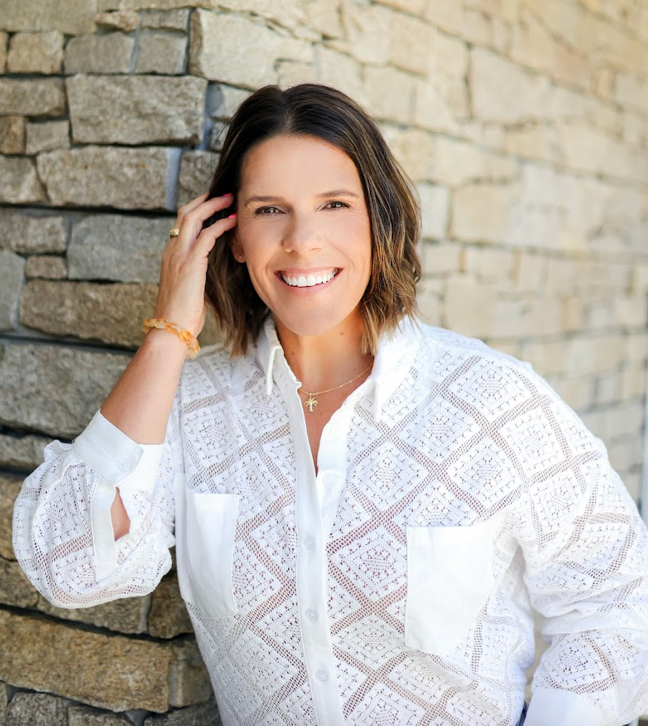 Community and Family Studies (CAFS) and education coach Kelly Bell in a aqua jacket holding a microphone,, smiling and raising her hand in wave