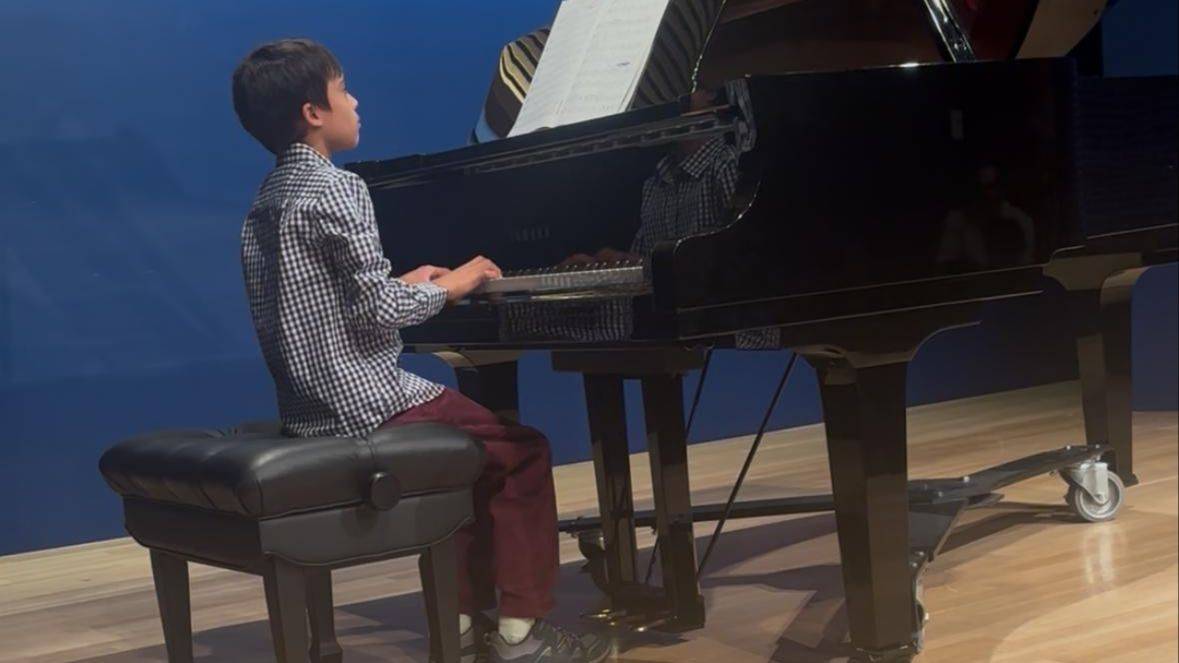 Young pianist performing at a grand piano from a side angle