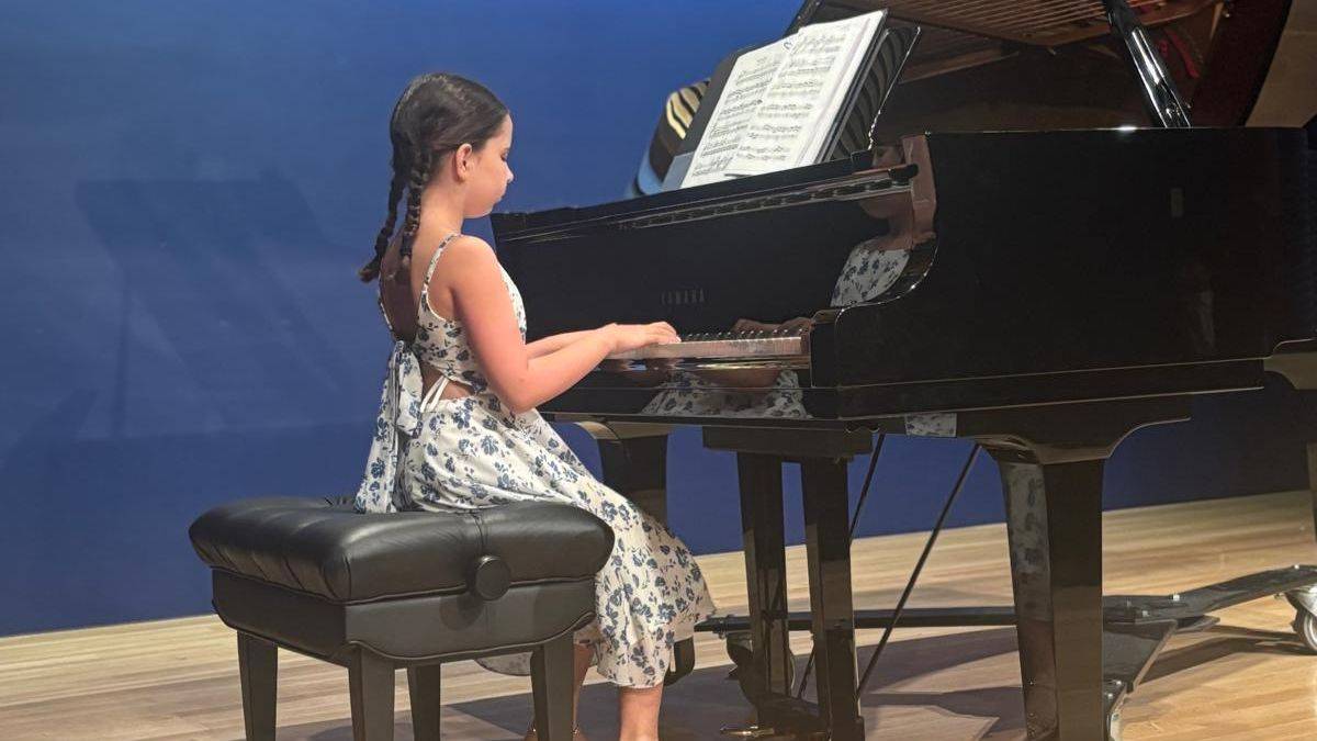 Young pianist in a floral dress performing at a grand piano