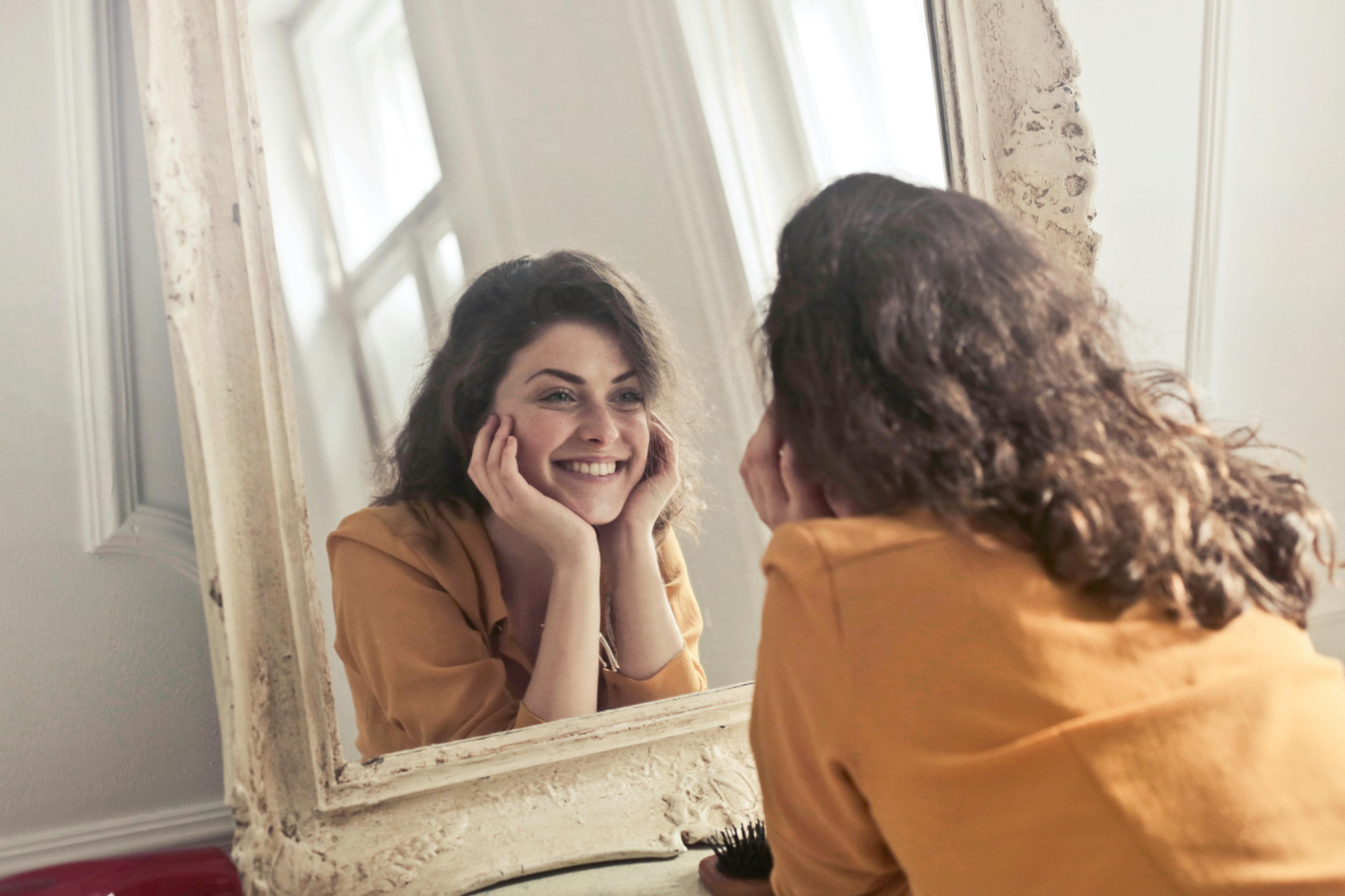 Young adult woman smiling at herself in the mirror during a moment of self-reflection and confidence building