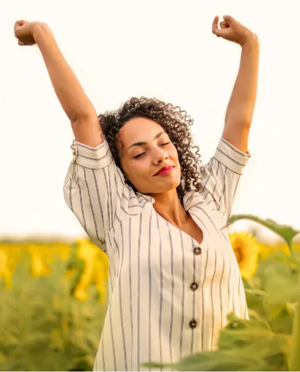 Woman with arms raised joyfully in a sunflower field representing self-nurturing and coming back to yourself