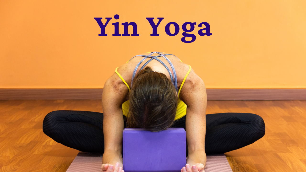 Woman practicing yin yoga in a forward-fold pose with her forehead resting on a yoga block in a calm orange-walled studio — illustrating gentle, restorative yoga used for emotional release and mindfulness.