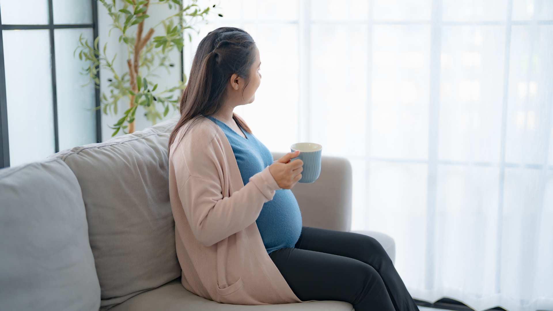 Pregnant woman sitting with a mug by the window, representing perinatal mental health support, antenatal anxiety and emotional wellbeing.
