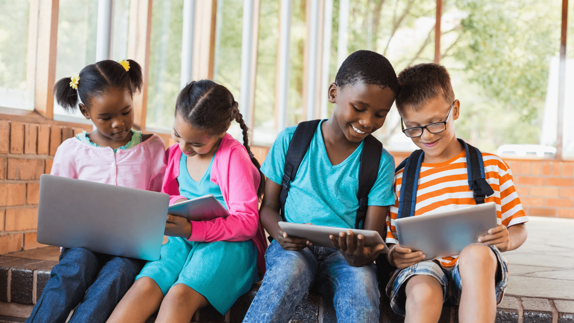 Four happy and engaged kids, smiling about the work they're doing on their shared devices