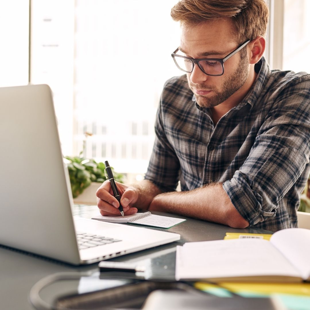 An NDIS provider refining his messaging to incorporate his unique skills into his offers. man sitting at desk writing near his laptop