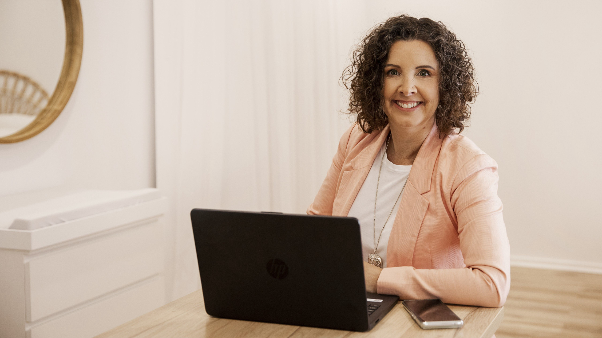 A woman sitting at a desk smiling in front of a laptop