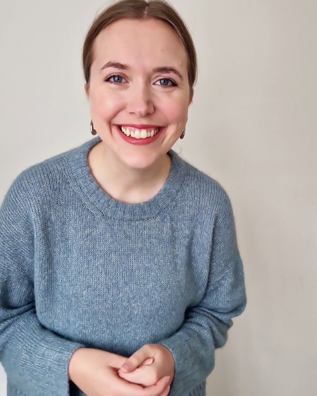 Photo of Clare wearing a handknit slipover and gazing at the camera warmly