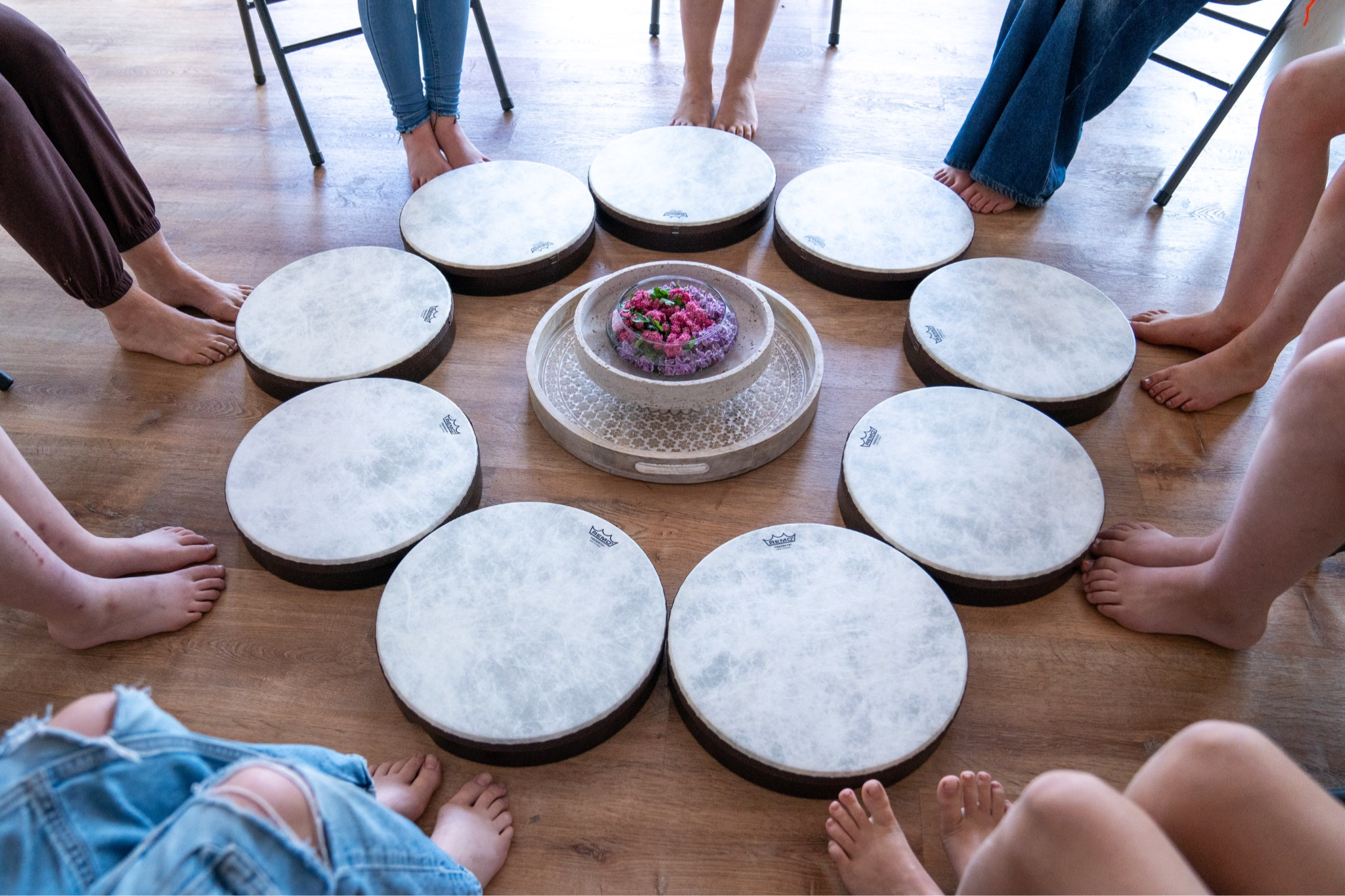 picture of girls feet in a circle with frame drums and flowers in the middle with frame drum teacher Krista Holland 