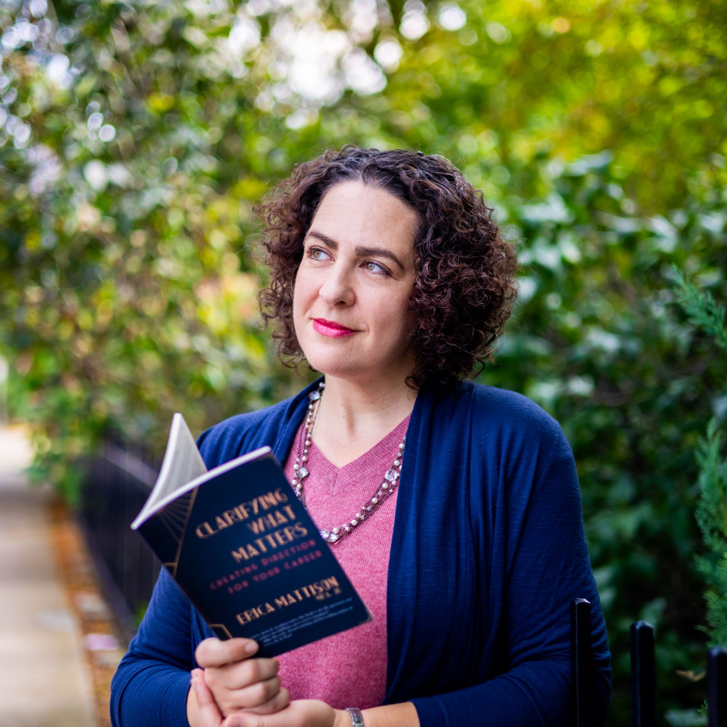 Erica Mattison holding her book Clarifying What Matters career clarity guide, looking up pensively