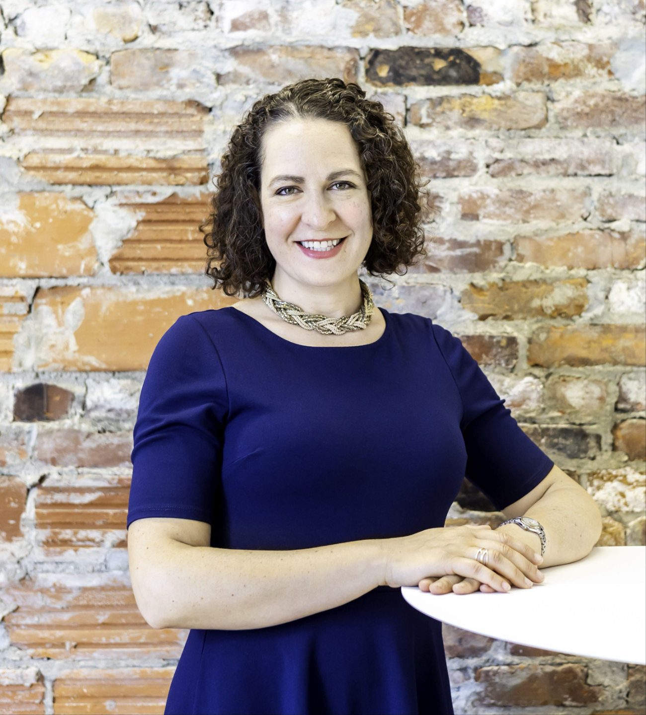 Erica Mattison wearing navy blue, smiling, in front of a rustic brick wall