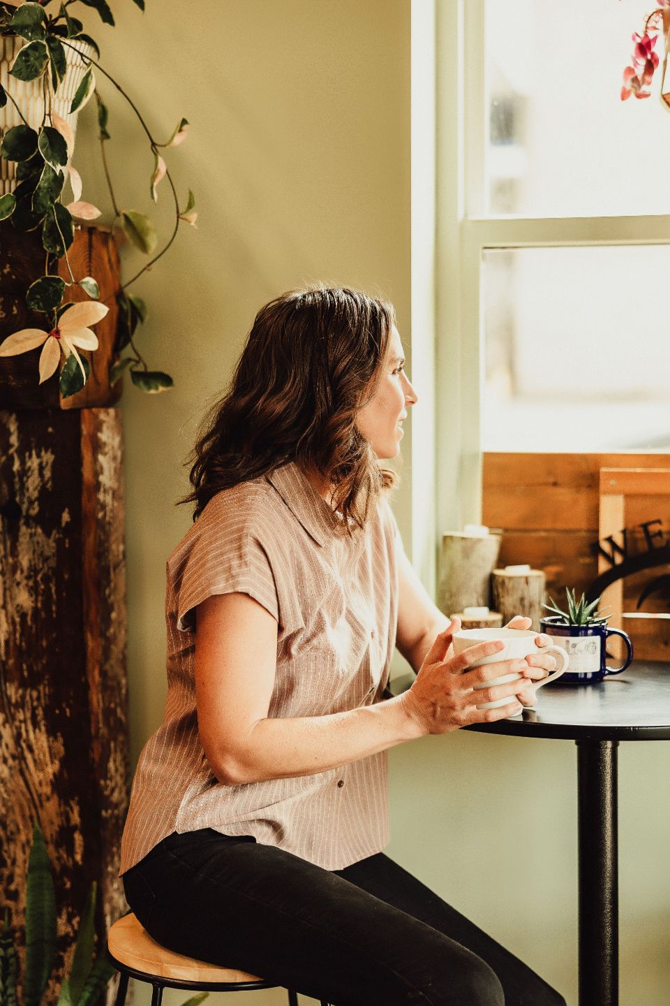 Woman sitting by a window with coffee, reflecting and building mindful habits