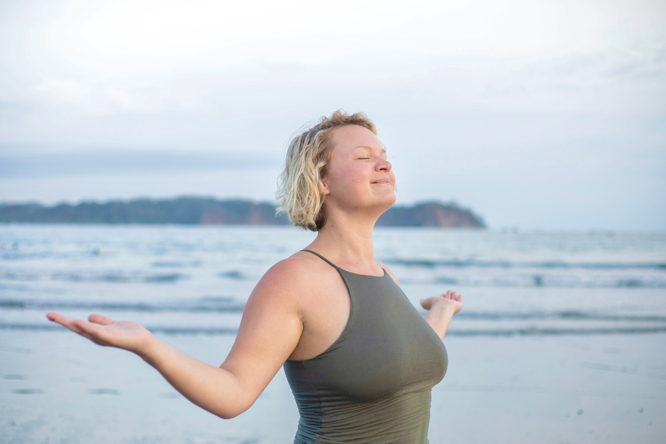 woman smiling with eyes closed and head tilted towards the sky with arms spread, symbolizing a feeling of ease, peace, and joy