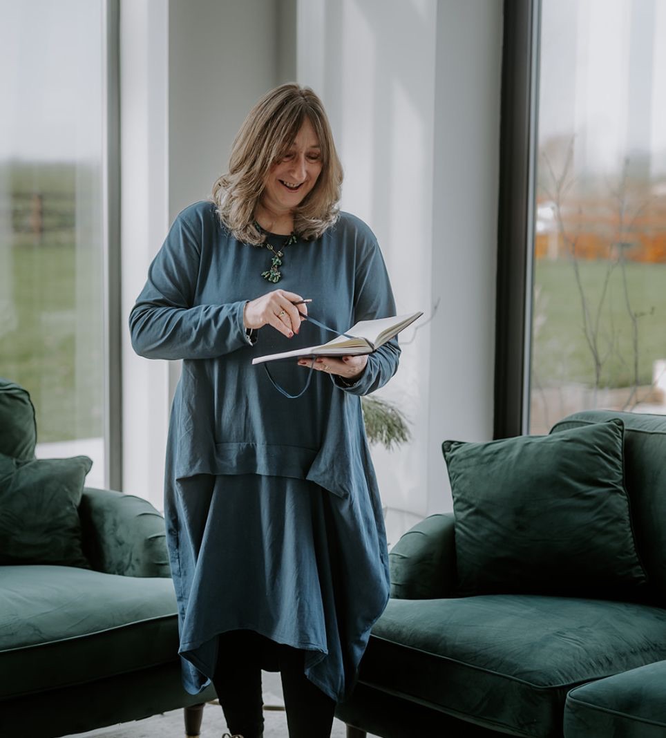 Elizabeth James smiling while writing in her notebook, offering calm private WhatsApp mentoring for baby class teachers