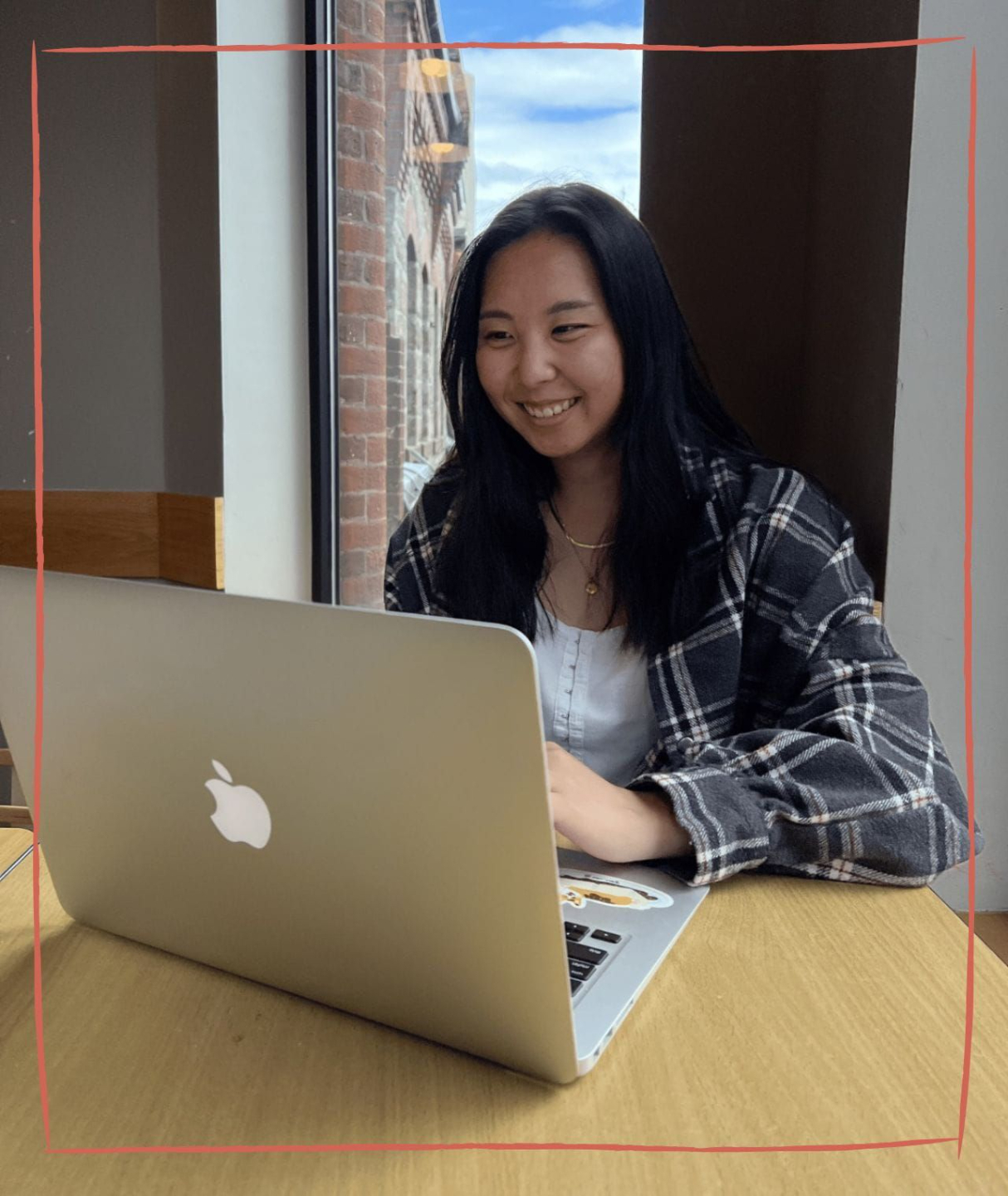 Someone wirting in a notebook while also look at another book. A laptop and coffee mug are on their table.
