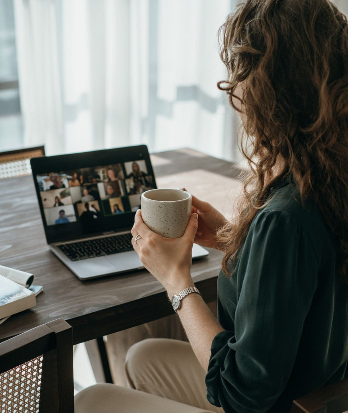 A woman with wavy hair in a white shirt and brown pants walks through a grassy field, surrounded by greenery and wildflowers.