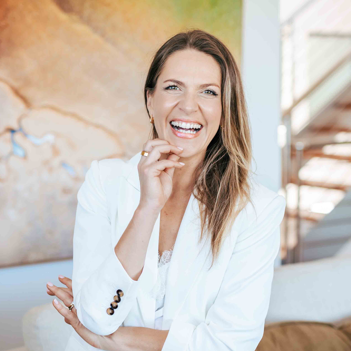 Picture of Clinical Psychologist, Mariane Power, who is smiling and wearing a crisp white shirt and blue jeans, sitting on a tan coloured sofa and holding a book called Life is Good