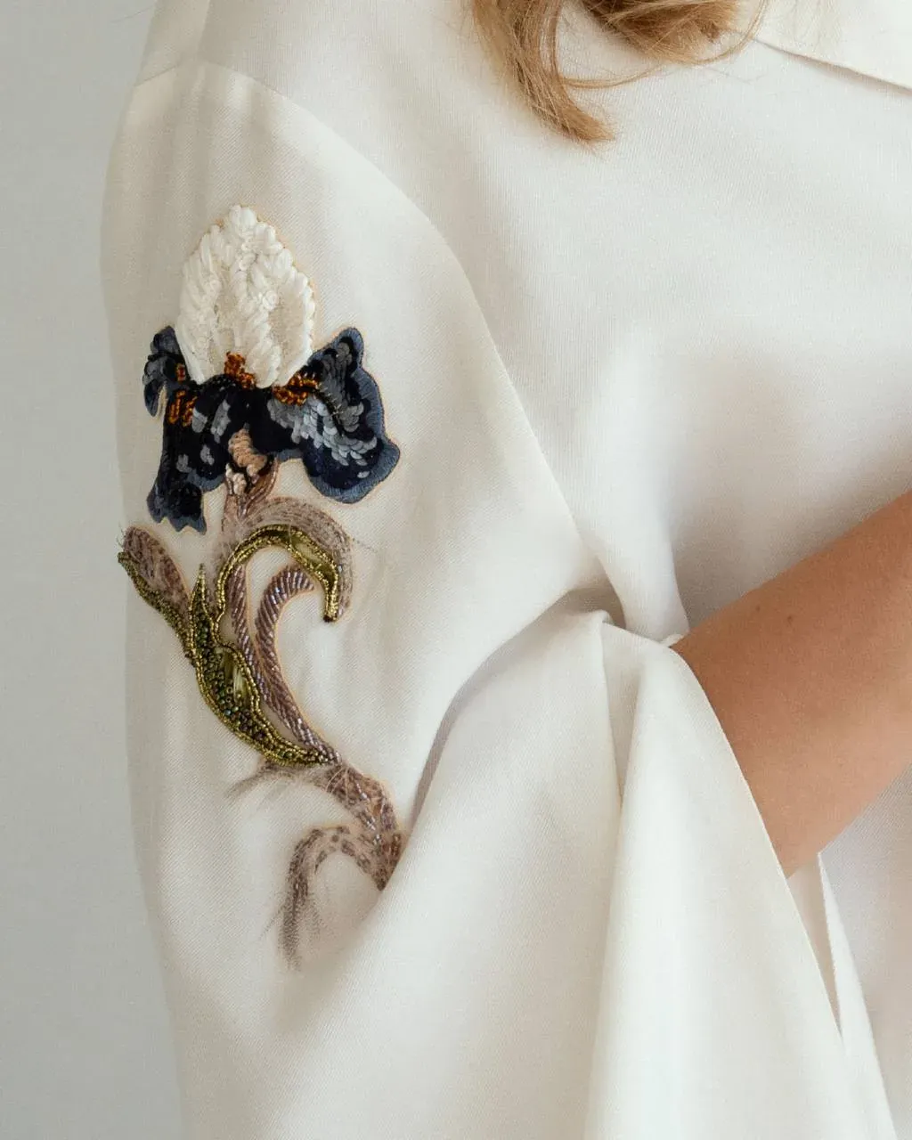 Floral embroidered brooch on a white blouse sleeve, couture embroidery by Greta of GUNI Design Studio