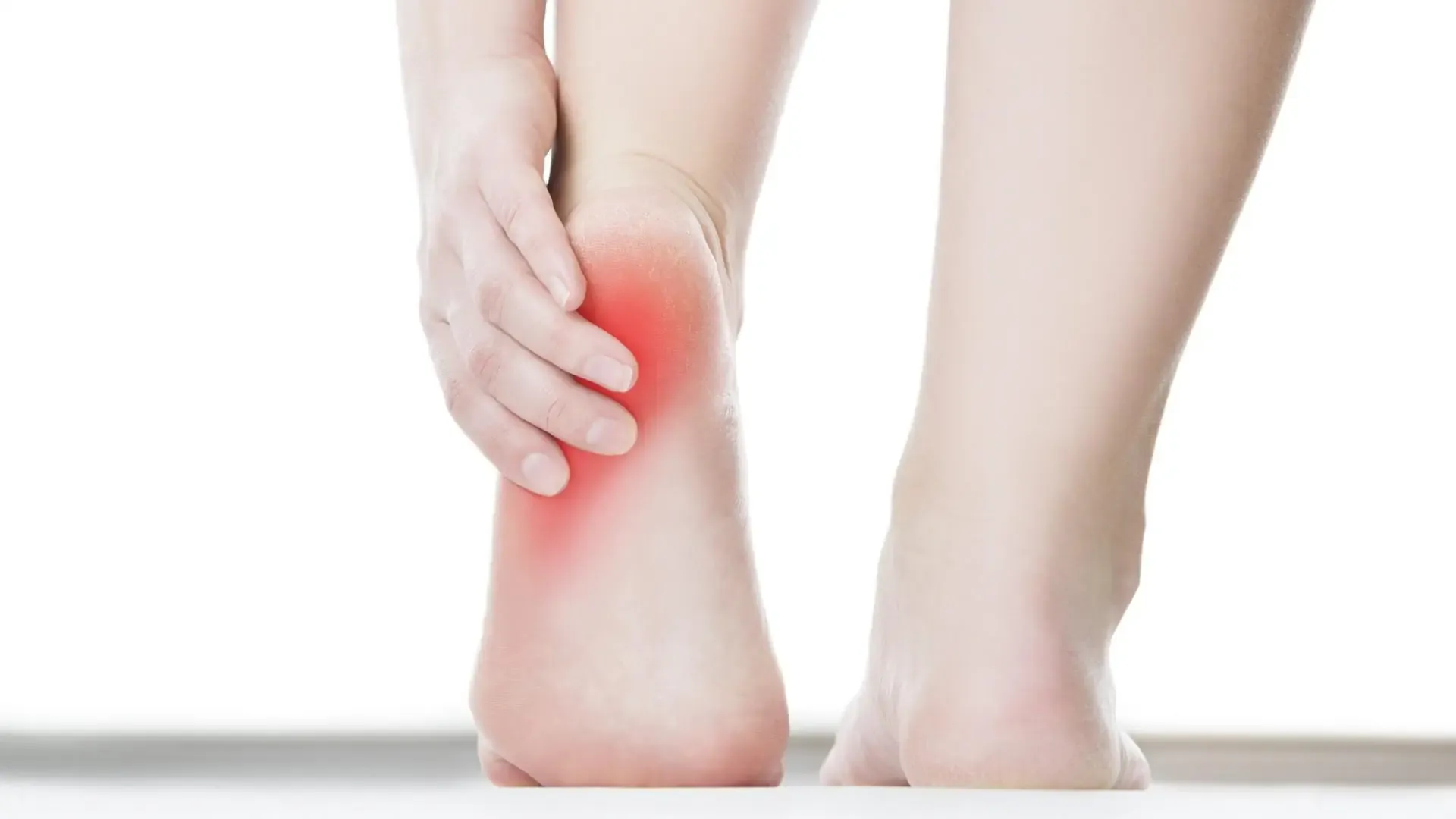 Person standing, holding one heel in pain with both feet visible
