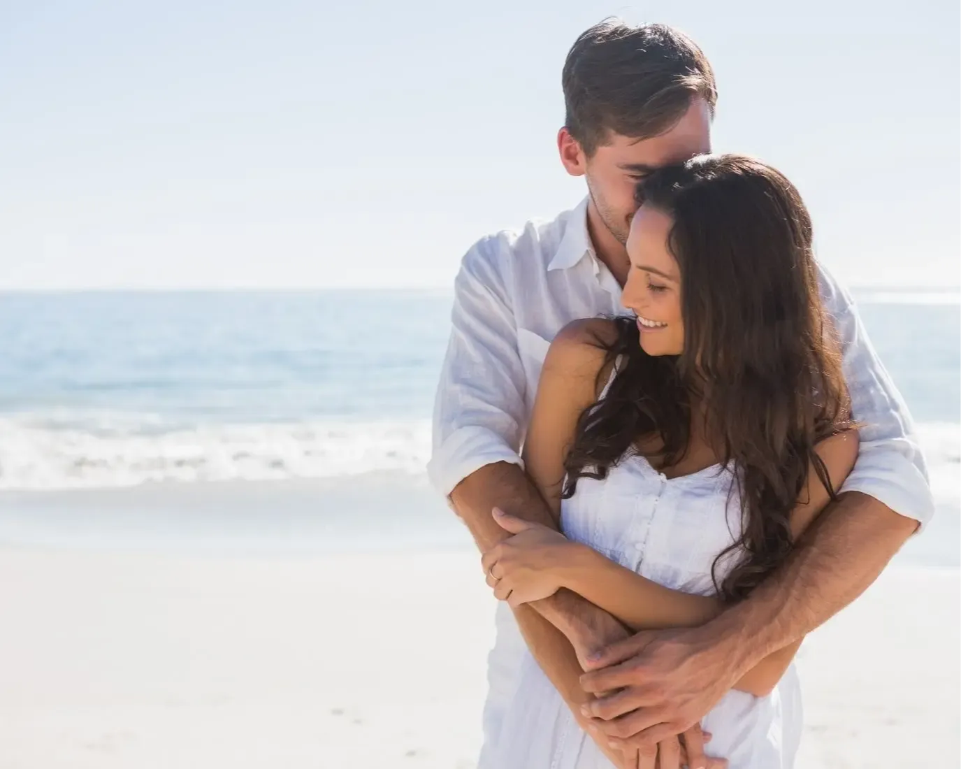 happy couple in love holding one another on a beach with ocean behind them