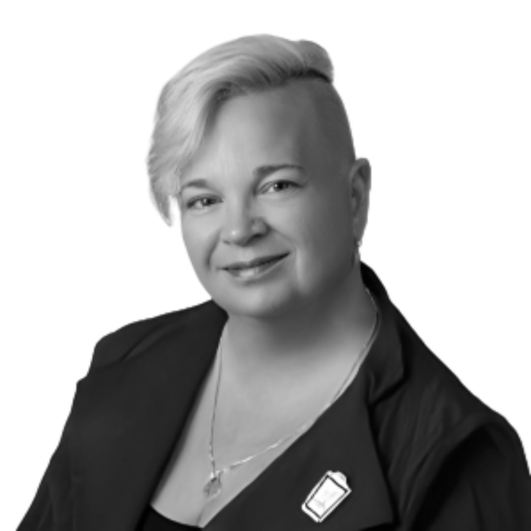 Smiling woman with short asymmetrical haircut wearing a blazer and necklace, posed against a plain background
