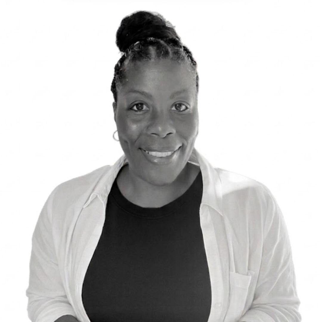 Smiling woman with braided hair in a bun, wearing a black top and light jacket, facing forward against a plain background