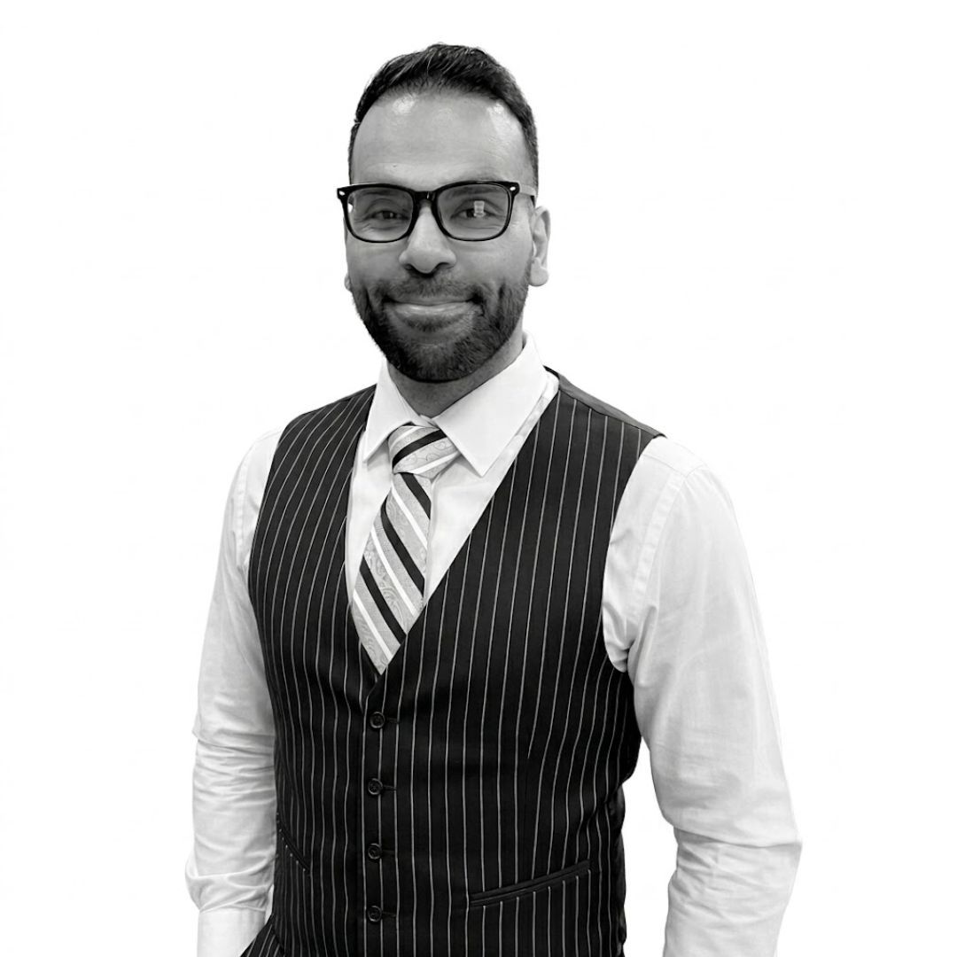 Smiling man wearing glasses, a striped vest, white shirt, and tie, posing against a plain background