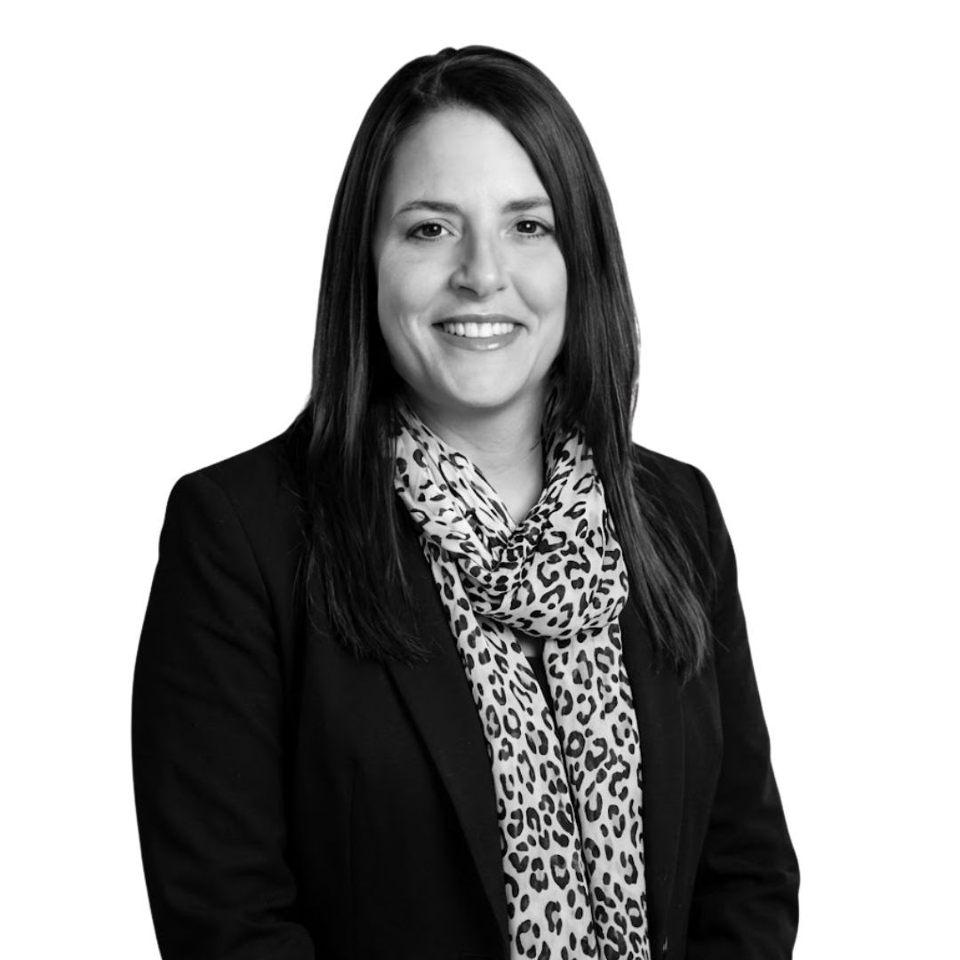 Smiling woman with long straight hair wearing a black blazer and patterned scarf, facing forward against a plain background