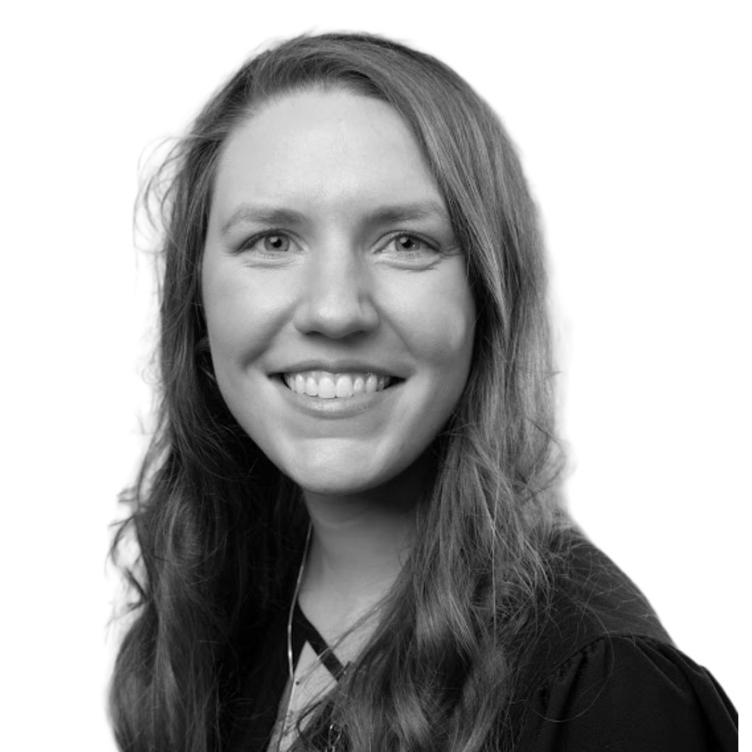 Smiling woman with long wavy hair wearing a dark top, facing slightly to the side against a plain background