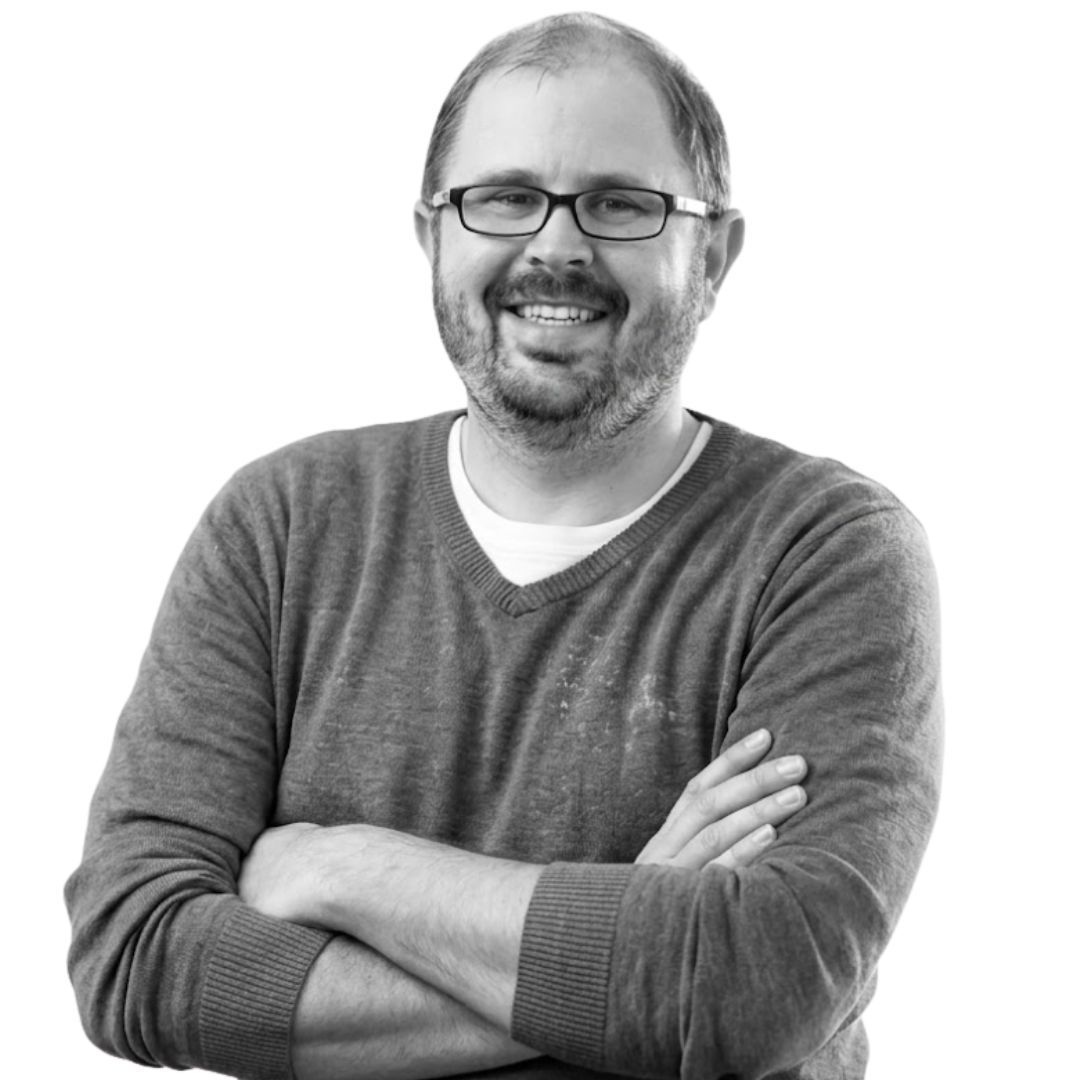 Smiling man with glasses and short hair, wearing a casual sweater with arms crossed, facing forward against a plain background