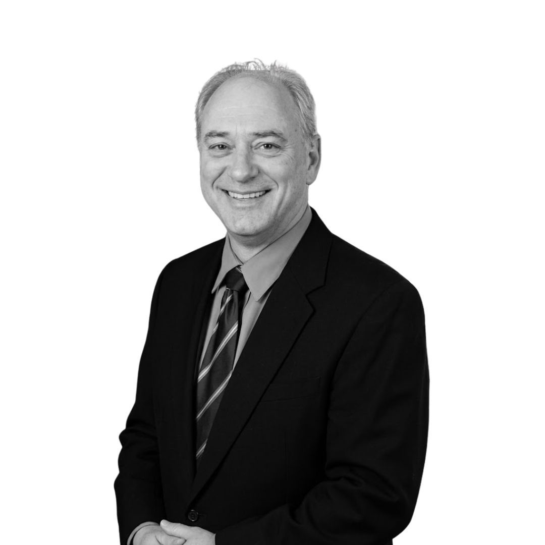 Smiling man with short hair wearing a suit and tie, facing forward against a plain background