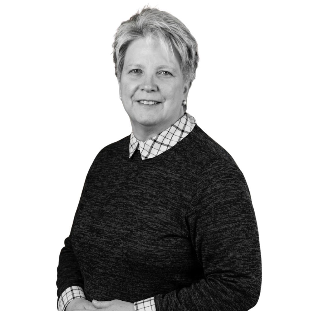 Smiling woman with short hair wearing a dark sweater over a collared shirt, facing forward against a plain background