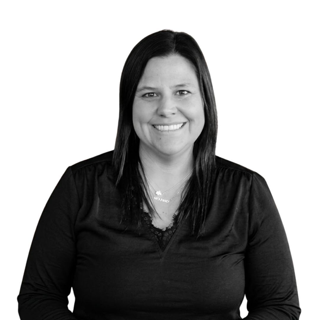 Smiling woman with long straight hair wearing a black blouse and necklace, facing forward against a plain background