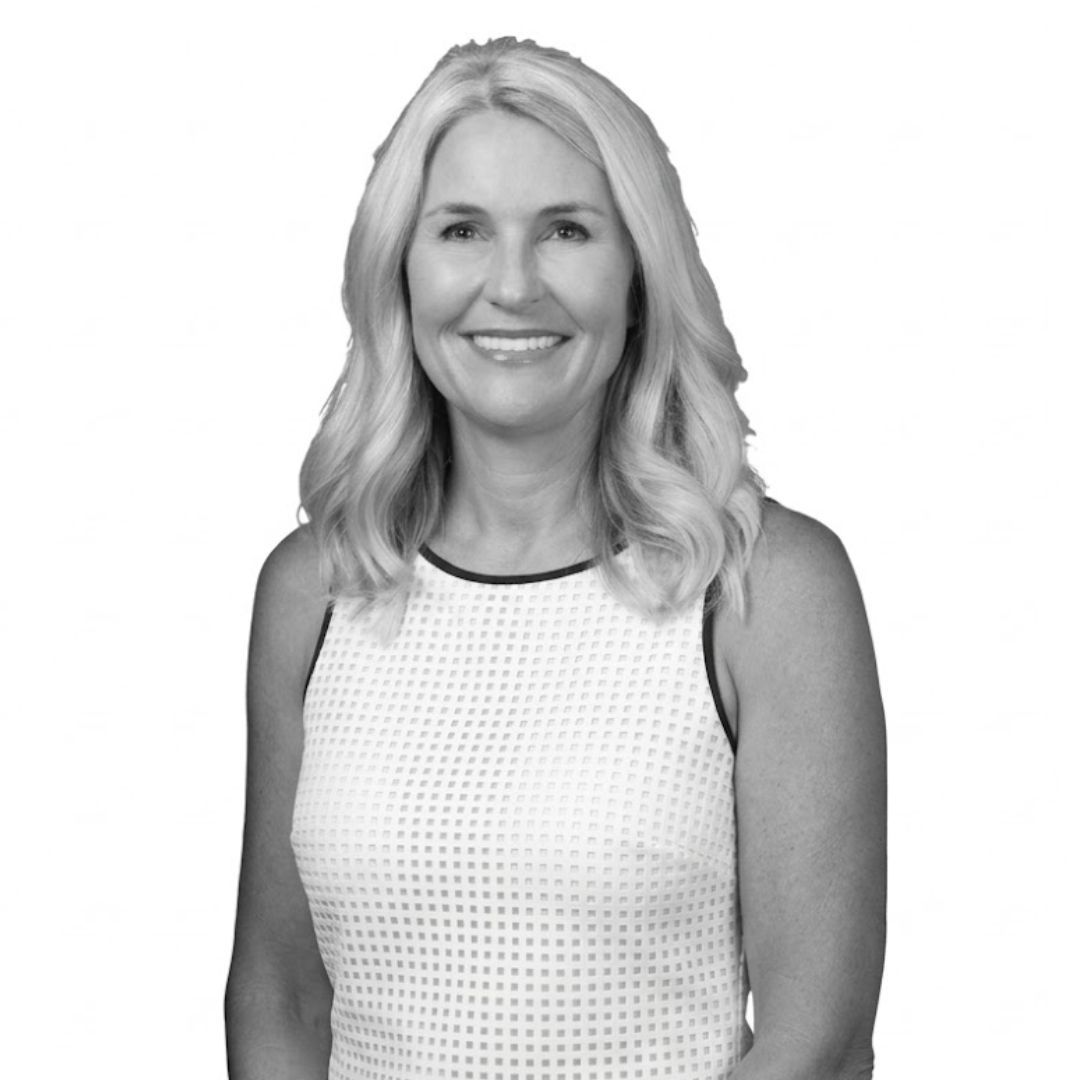 Smiling woman with shoulder-length wavy blonde hair wearing a sleeveless textured top, facing forward against a plain background