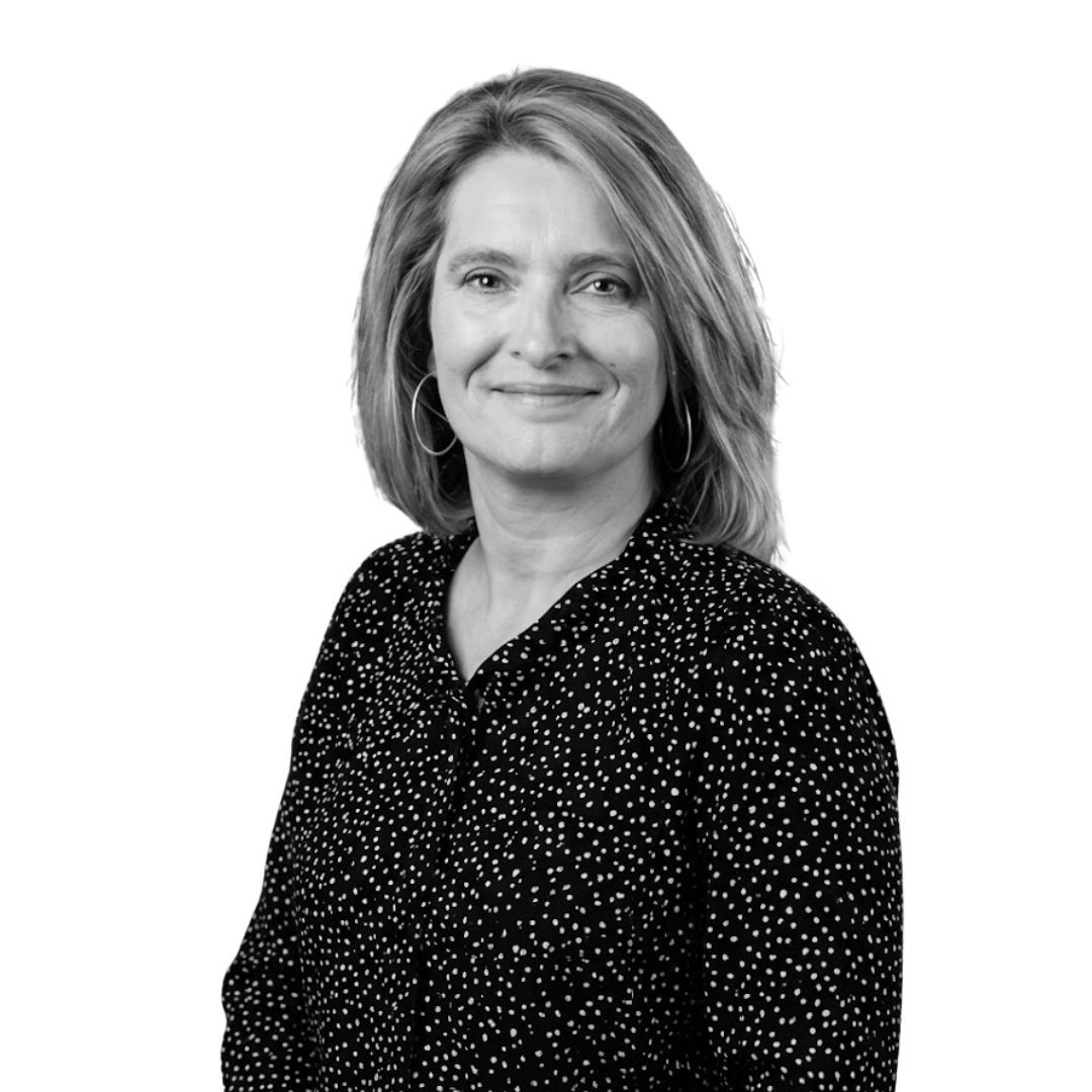 Woman with shoulder-length straight hair wearing hoop earrings and a patterned blouse, facing forward against a plain background with a slight smile
